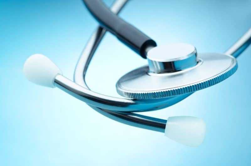 Close-up of a stethoscope on a blue background, with focus on the metal chestpiece and white earpieces.