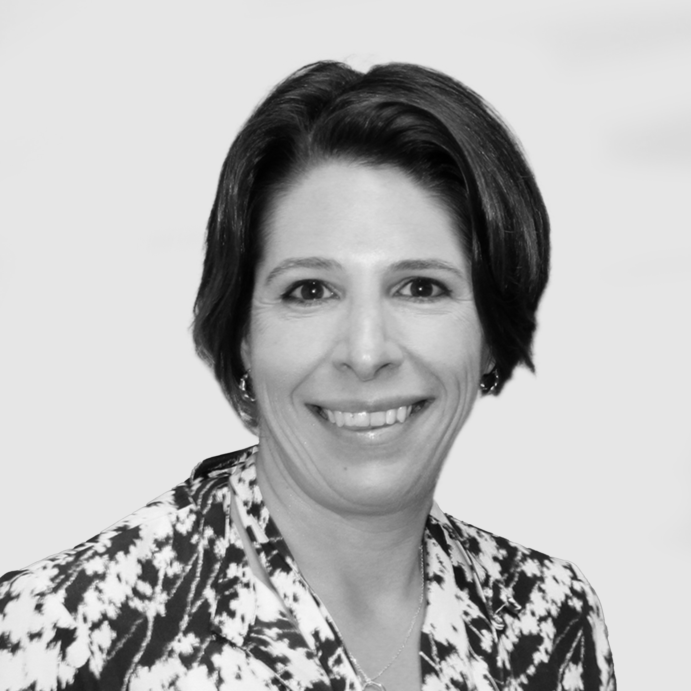 Smiling woman with short dark hair, wearing a patterned jacket, photographed against a plain light background.