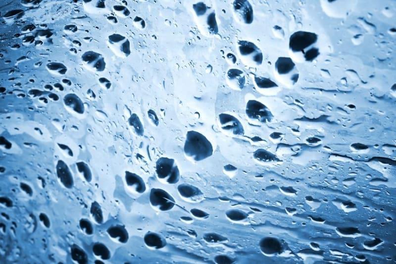 Close-up of numerous water droplets on a glass surface, with a blue tint and light shining through, creating patterns and texture in the liquid.