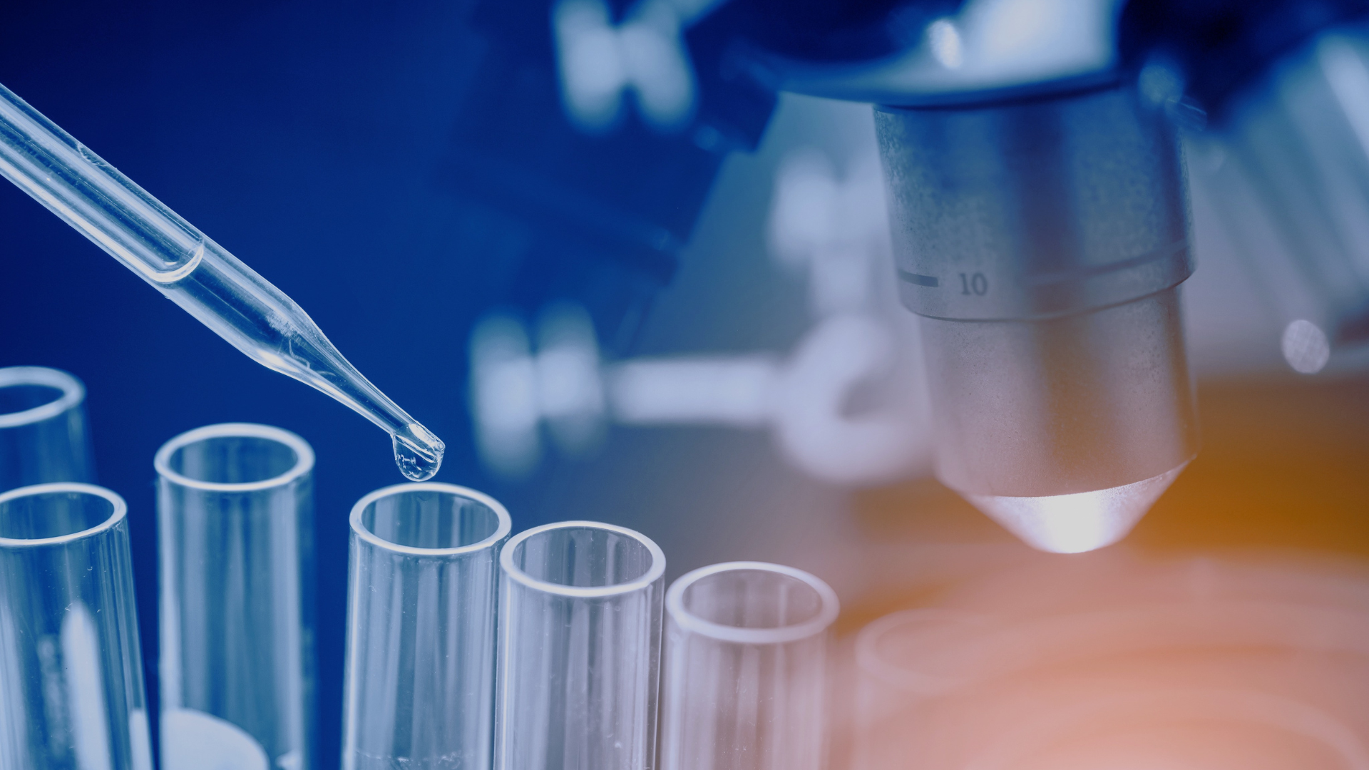 A pipette releases liquid into glass test tubes beside a microscope, representing a laboratory science experiment with a blue and orange colour tone.