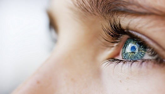 Close-up of a person's face focused on a blue eye with long lashes, reflecting light. The image captures detailed textures of the skin and eyebrow.