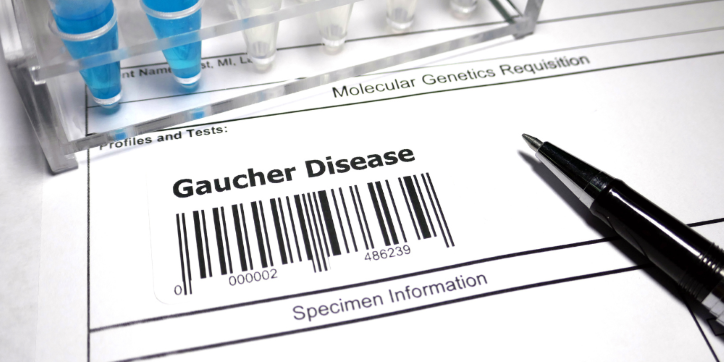 A medical form labelled Gaucher Disease with a barcode, a black pen, and blue-capped laboratory tubes in the background. The form is titled Molecular Genetics Requisition.