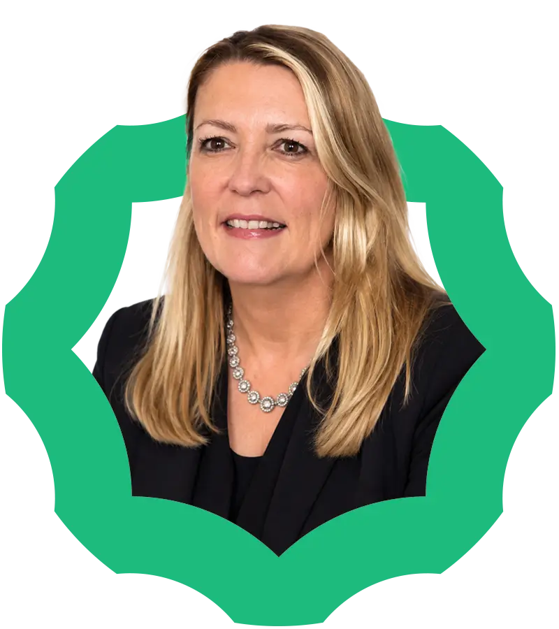 A woman with long blonde hair, wearing a black blazer and a silver necklace, is smiling. A green, decorative border frames her portrait.