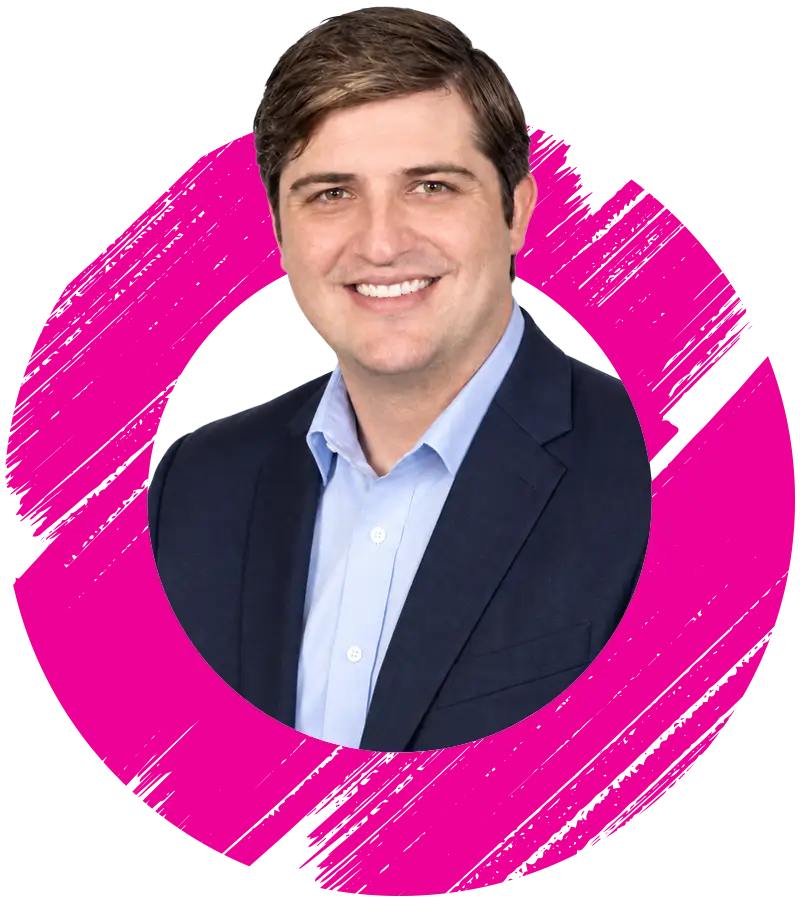A man with short brown hair, wearing a navy blazer and light blue shirt, smiles in front of a white background with a bold pink brushstroke circle design.