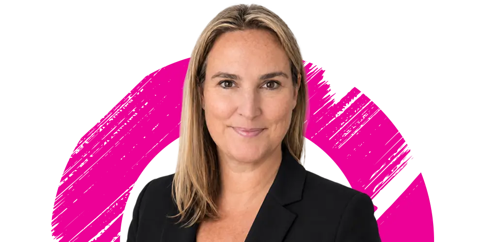 A woman with straight blonde hair, wearing a black blazer, smiles at the camera. The background features a pink brushstroke circle on white.