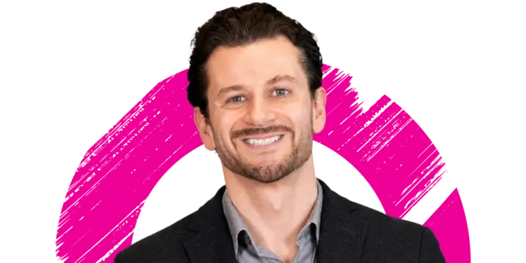A man with dark hair and a beard, wearing a dark blazer and light shirt, smiles in front of a white background with a pink circular brushstroke design.