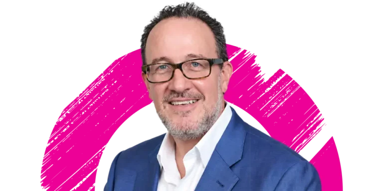 Smiling man with glasses and a beard in a blue suit and white shirt, in front of a white background with a bright pink brushstroke circle.