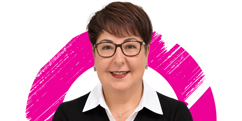Smiling woman with short brown hair and glasses, wearing a white collared shirt and black jumper, stands in front of a white background with a bold pink circular brushstroke design.