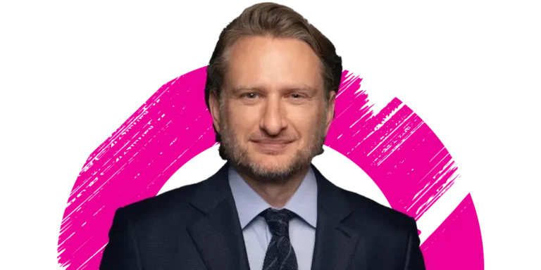 A man in a dark suit and tie smiles slightly, standing in front of a white background with a bold pink brushstroke circle behind him.