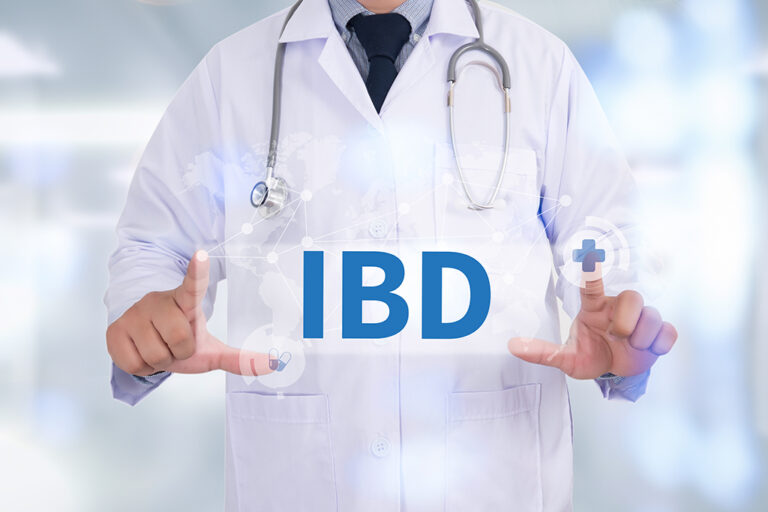 A doctor wearing a white coat and stethoscope holds up a digital panel with IBD written on it, representing inflammatory bowel disease awareness in a medical setting.