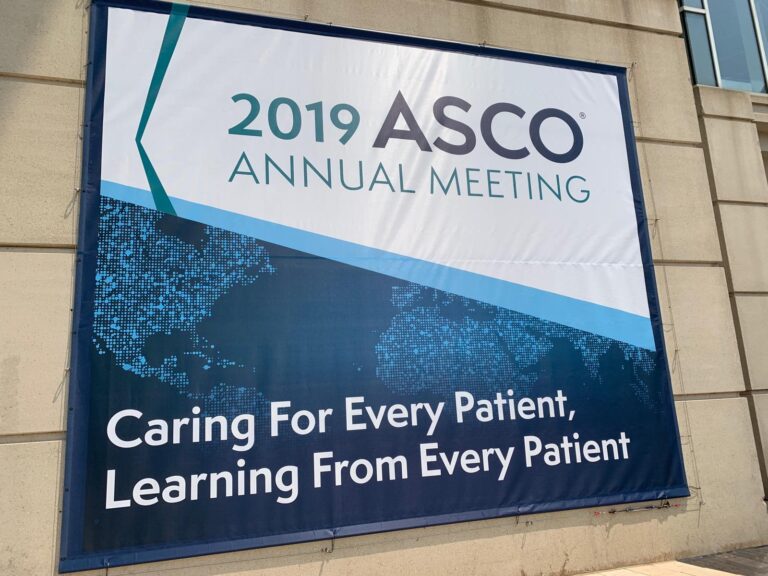 Banner for the 2019 ASCO Annual Meeting with the slogan, Caring For Every Patient, Learning From Every Patient, displayed on a building wall.