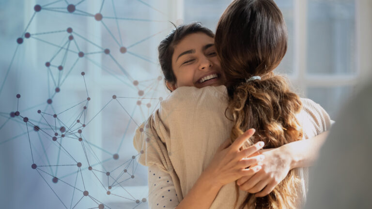 Two women hug and smile warmly, standing by a sunlit window. A network of interconnected lines and dots is faintly visible in the background.