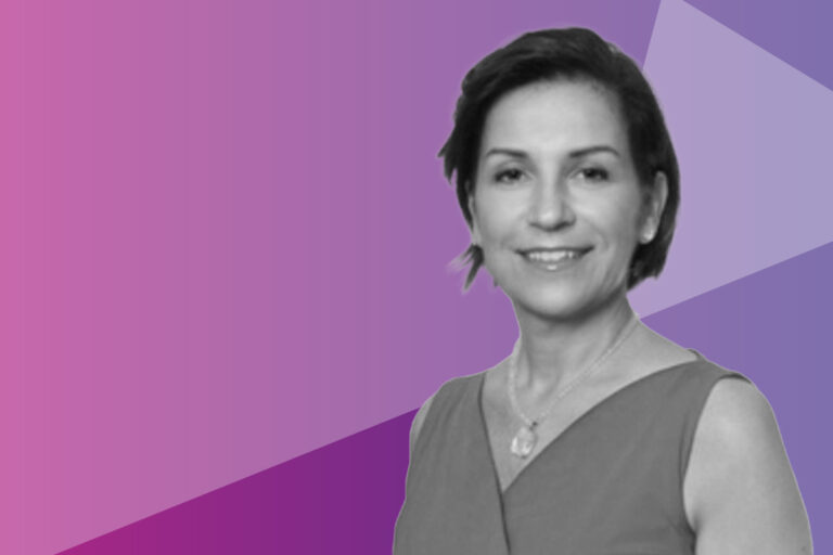 A woman with short hair smiles, wearing a sleeveless top and necklace, in front of a pink and purple geometric background.