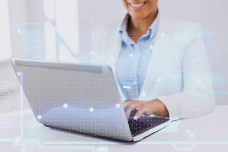 A person in a white blazer smiles whilst typing on a laptop, with futuristic digital graphics overlaid, symbolising technology and innovation.