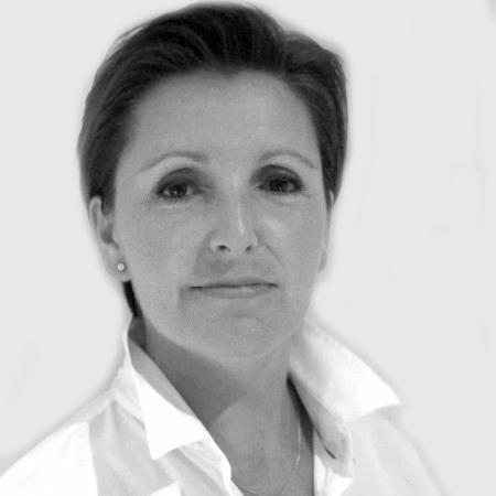 Black and white portrait of a person with short hair, wearing a white collared shirt, looking directly at the camera with a neutral expression against a plain background.