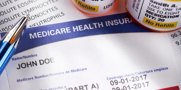 A Medicare health insurance card for John Doe is shown with prescription bottles and medical paperwork in the background.