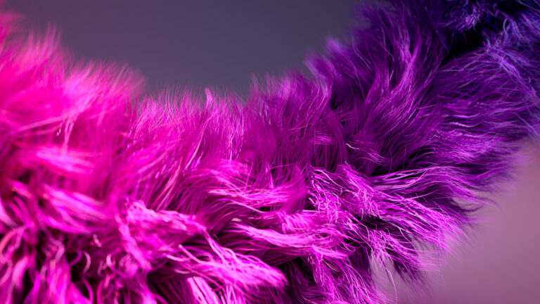 Close-up of vibrant, fluffy, pink and purple synthetic fibres or fur, with fine strands creating a textured and wavy appearance against a softly blurred background.