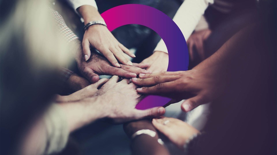 Several diverse hands are stacked together in a gesture of unity, with a purple semicircle graphic overlying the image.