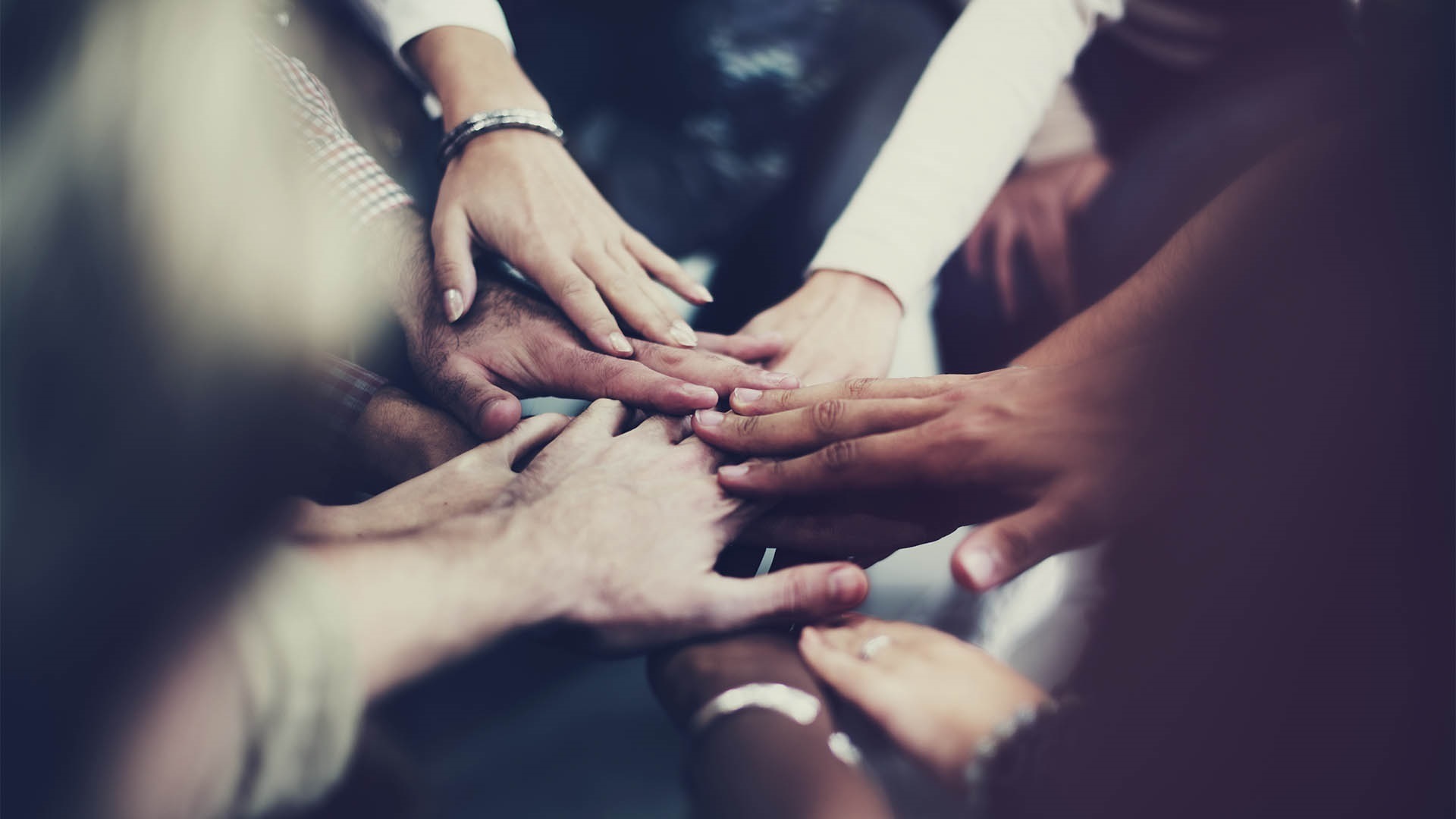 A group of diverse hands stacked together in the centre, symbolising unity, teamwork, and cooperation.