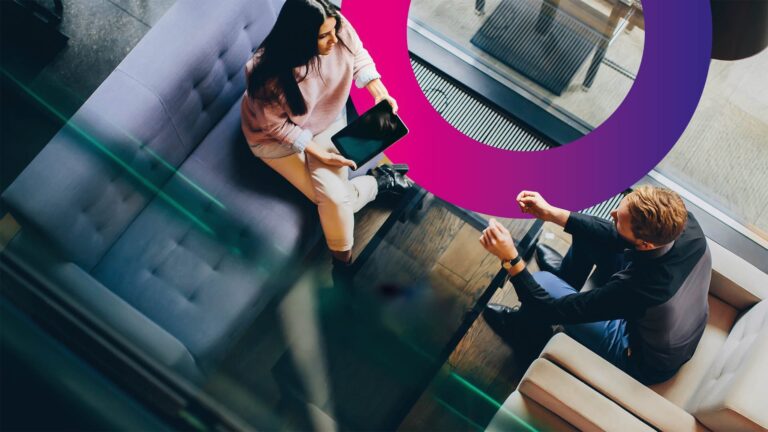 Two people sit opposite each other in a modern office lounge, discussing something while one person holds a tablet. The photo is taken from above, with a purple circular graphic over part of the scene.