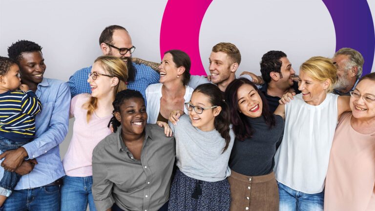 A diverse group of people of different ages and backgrounds stand together, smiling and laughing, with their arms round each other in front of a light background with coloured circles.