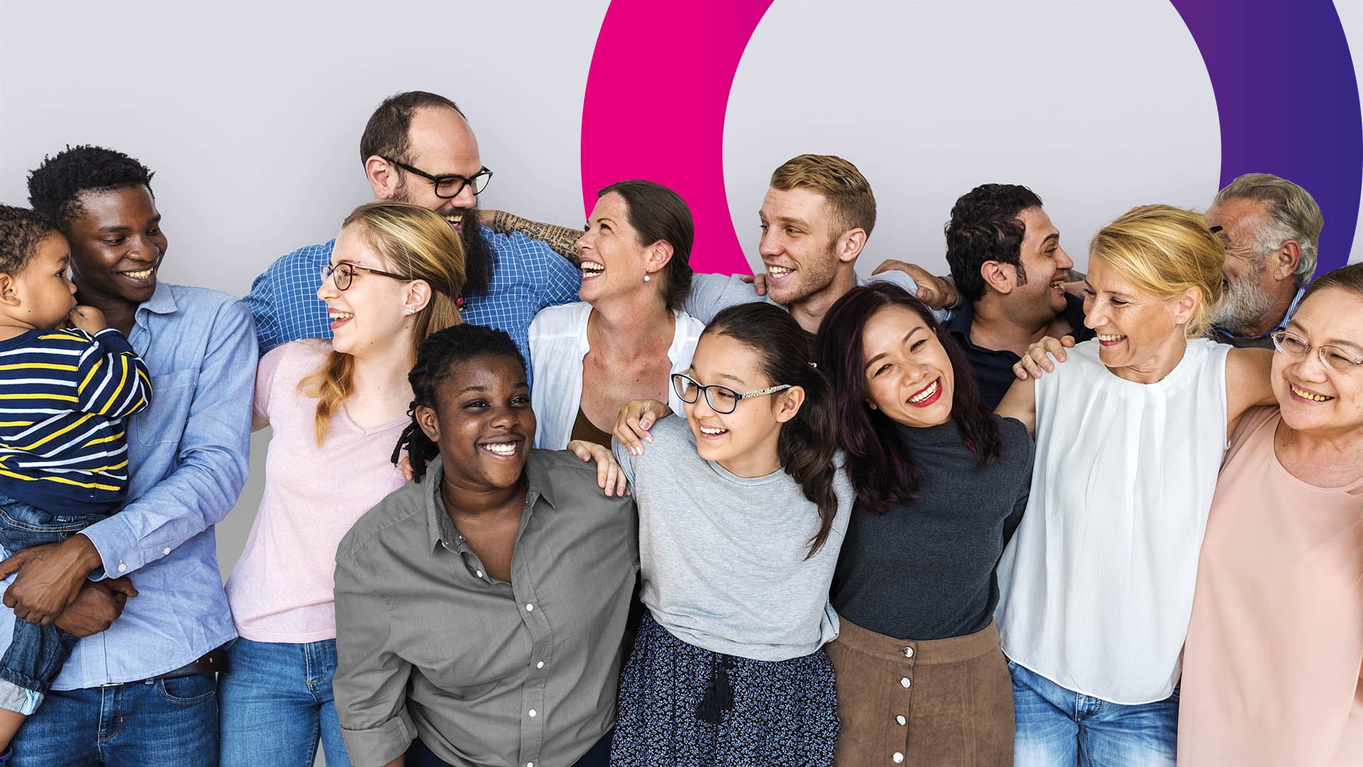 A diverse group of people of different ages and backgrounds stand together, smiling and laughing, with their arms round each other in front of a light background with coloured circles.