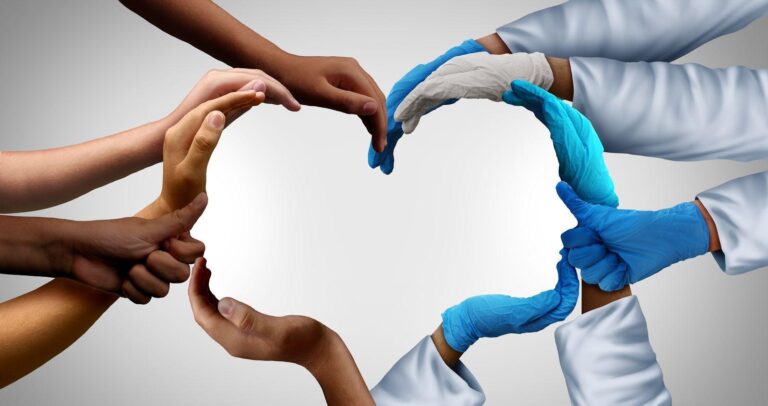 Several hands, some with medical gloves and lab coats, form the shape of a heart against a light background, symbolising unity, care, and teamwork in healthcare.