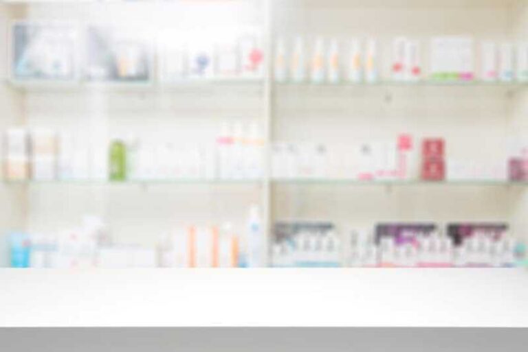 Blurred image of a chemist's shelf with various medicine boxes and bottles, with a white counter in the foreground.