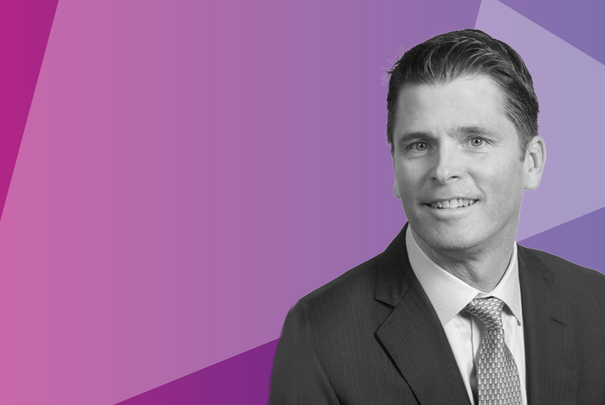 A man in a suit and tie is smiling, shown in black and white, against a vibrant, geometric purple and pink background.