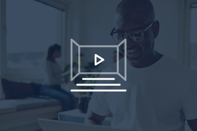 Smiling person in glasses using a laptop indoors, with two people talking in the background. A translucent video play button icon is overlaid on the image.