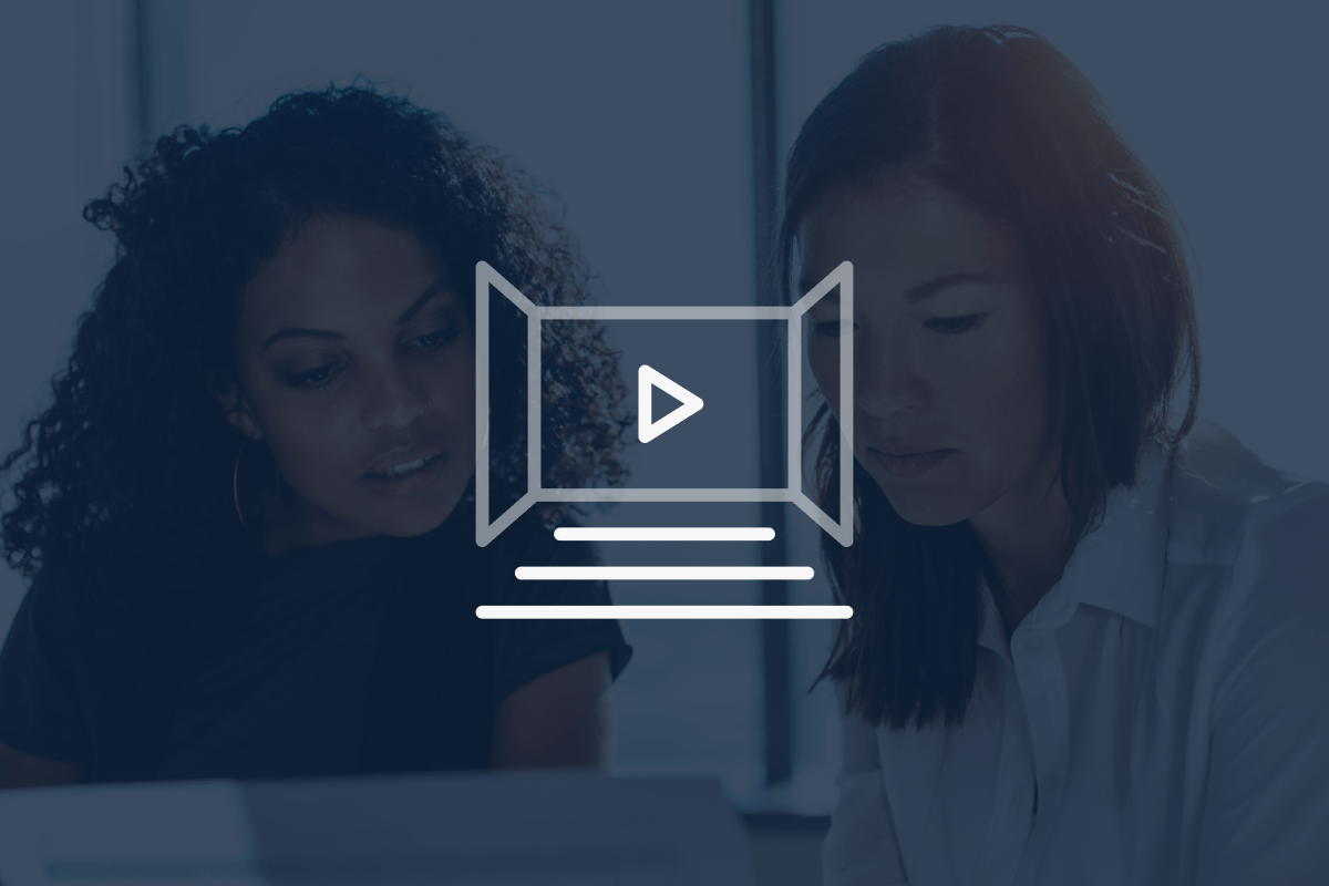 Two women sitting together and looking at documents, with a transparent play button and video icon overlay on top of the image.