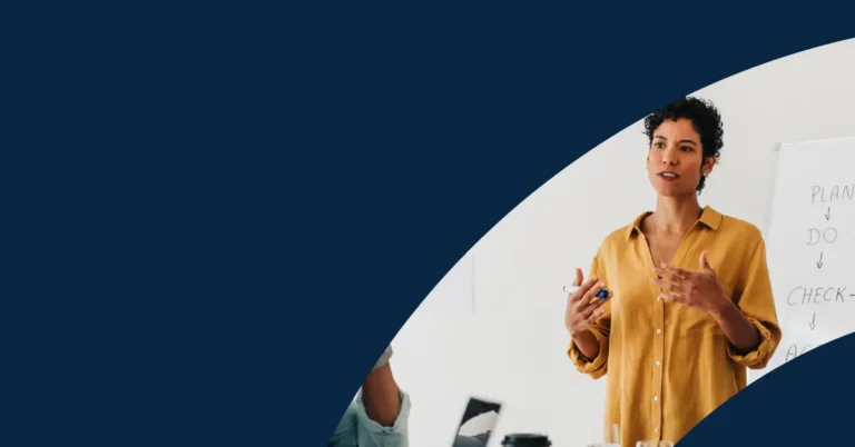 A person in a yellow shirt stands and speaks near a whiteboard with partially visible writing, in a room with a dark blue graphic overlay covering much of the image.