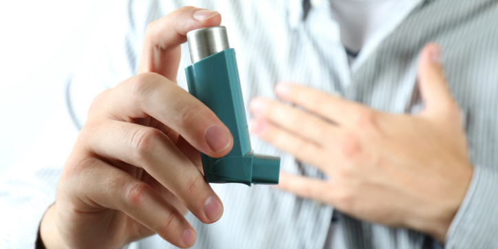 A person holding an inhaler in one hand and touching their chest with the other, suggesting difficulty breathing or asthma.