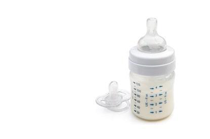 A baby bottle filled with milk sits beside a clear dummy on a white background.
