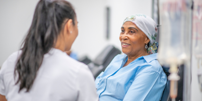 A woman wearing a headscarf smiles whilst sitting and talking with a healthcare professional in a medical setting.