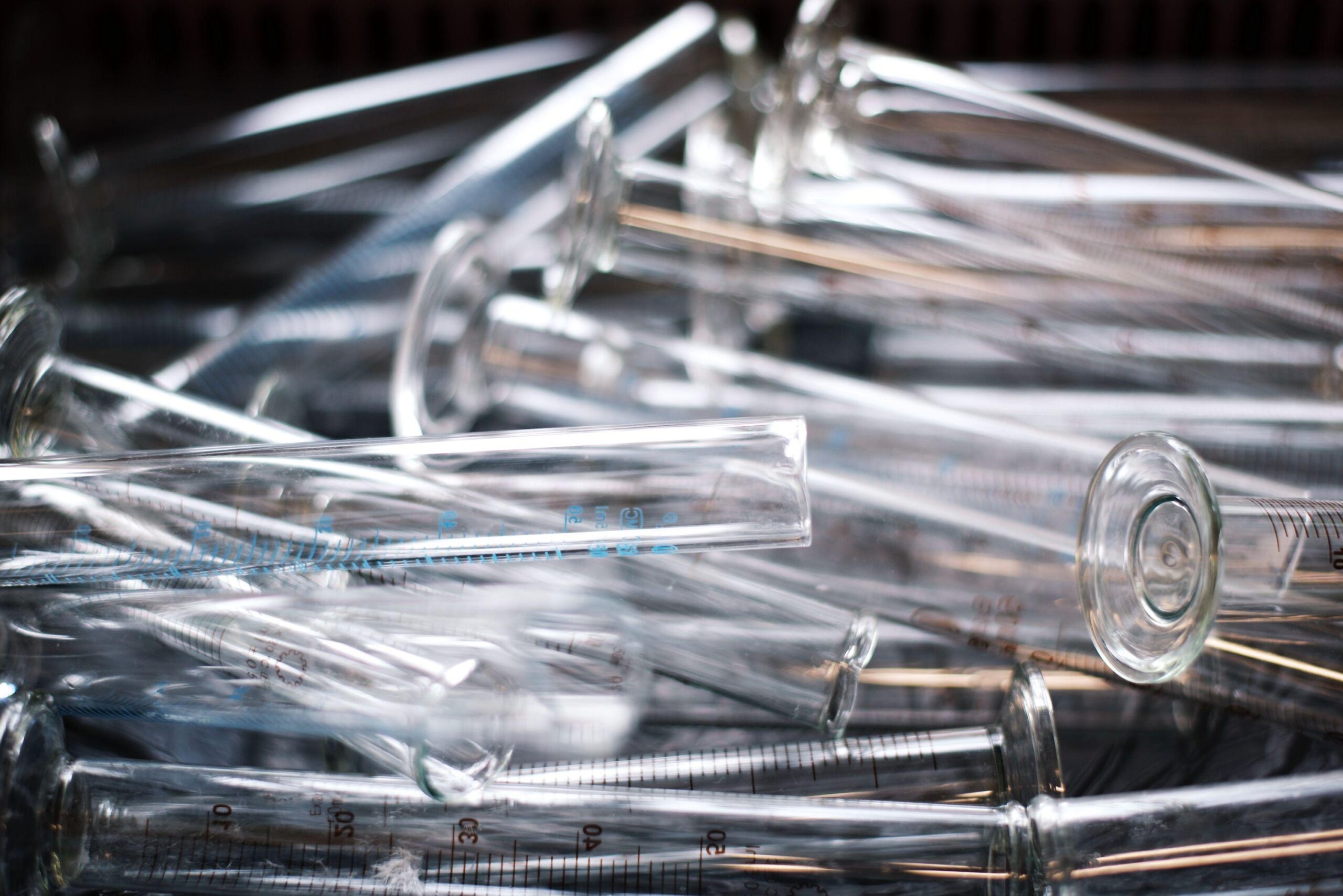A pile of clear glass graduated cylinders stacked closely together, some overlapping, with measurement markings visible on the sides.