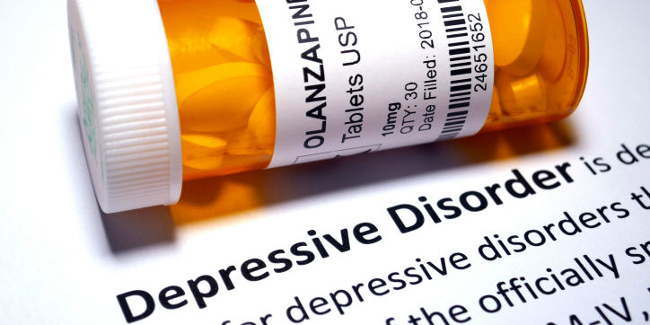 A prescription pill bottle labelled Olanzapine rests on a document that defines depressive disorder, with Depressive Disorder printed in bold text.
