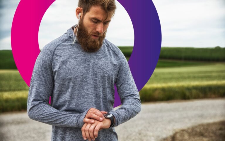 A man with a beard, wearing earphones and a grey athletic top, checks his smartwatch while standing outdoors near a field. A large purple and pink circle is in the background.