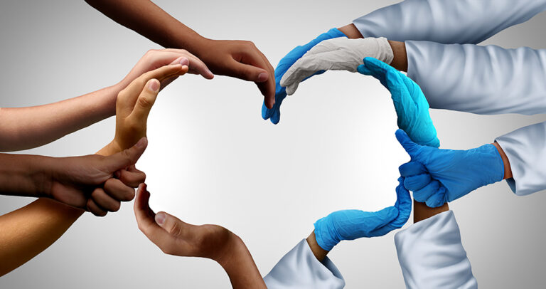Multiple hands, some gloved and some bare, form the shape of a heart against a light background, symbolising unity, healthcare, and teamwork.