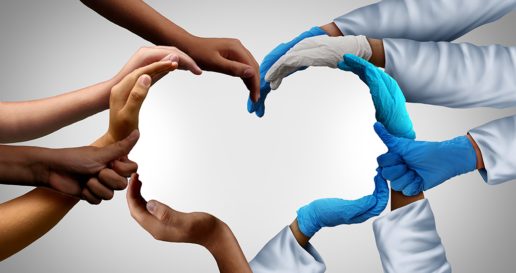 Multiple hands, some gloved and some bare, form the shape of a heart against a light background, symbolising unity, healthcare, and teamwork.