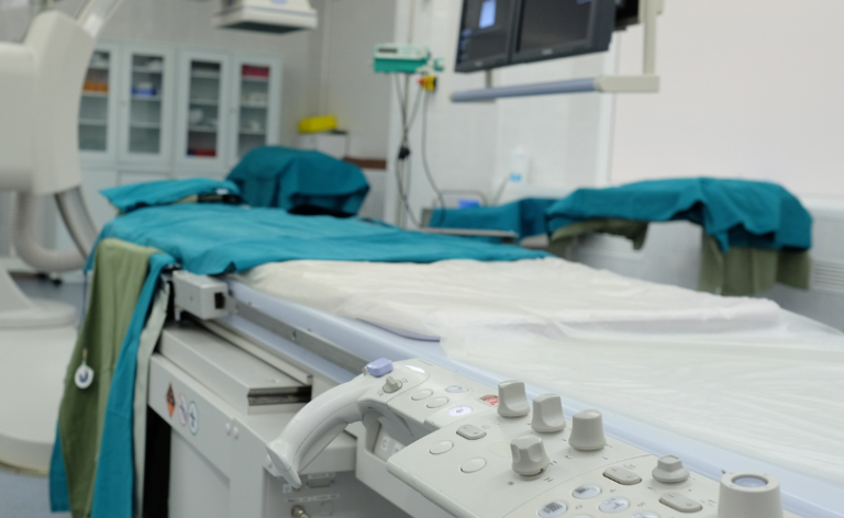 A hospital examination room with a covered medical bed, control panel, monitors, and medical equipment, prepared for a procedure.