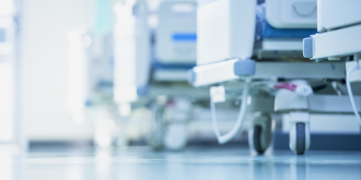 Close-up view of hospital beds on castors in a bright, clean corridor, with the image slightly out of focus, emphasising a clinical and sterile healthcare environment.