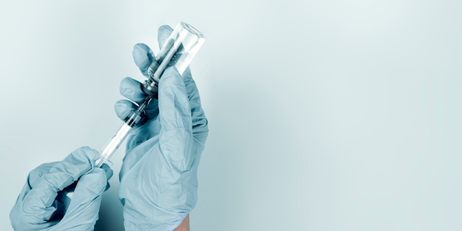 Gloved hands holding a vial and drawing liquid into a syringe against a light blue background.