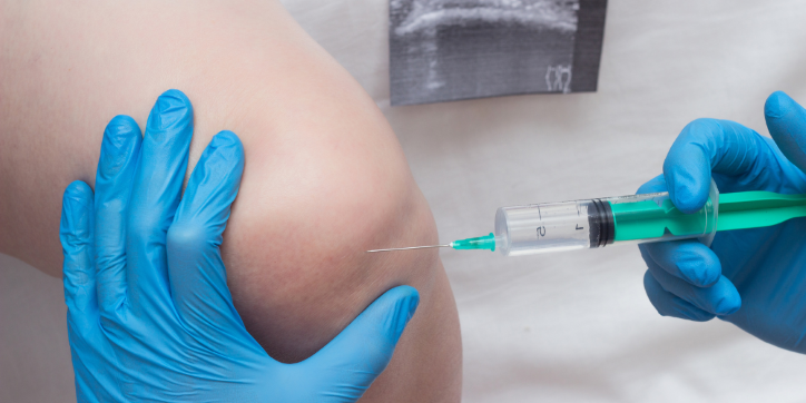 A medical professional wearing blue gloves prepares to inject a syringe into a patient's knee, possibly for treatment or pain relief. An X-ray image is visible in the background.