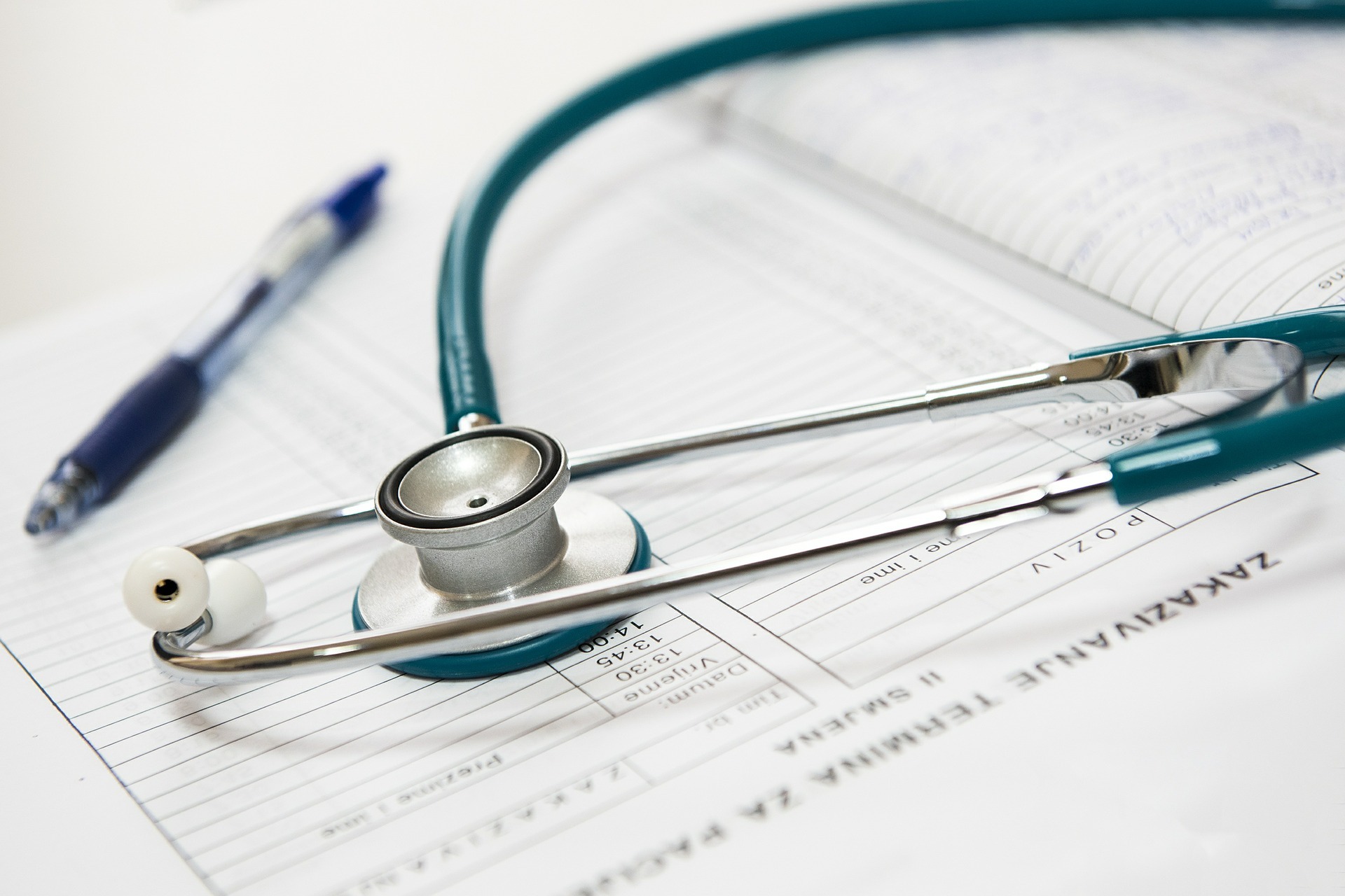 A stethoscope and a pen rest on a medical chart with handwritten notes and printed patient information.