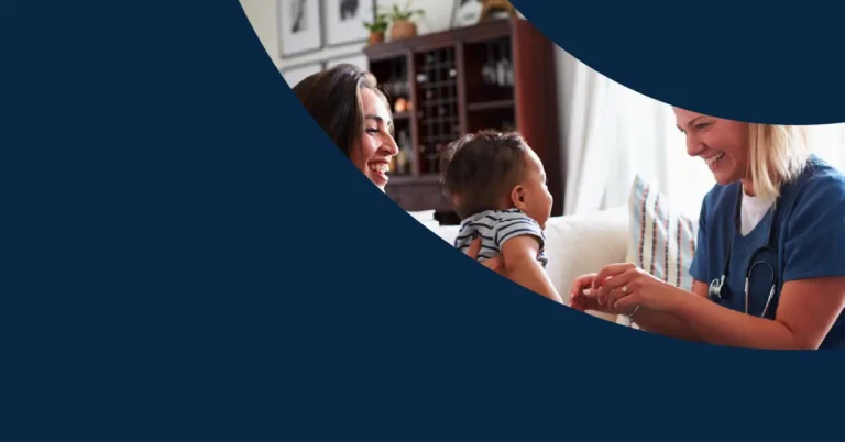 A nurse in blue scrubs smiles whilst interacting with a baby being held by an adult woman, with both adults appearing happy in a cosy living room. Navy blue shapes partially cover the image.