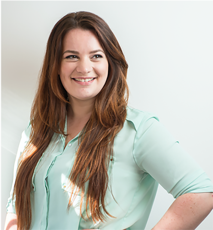 A woman with long brown hair, wearing a light green blouse, stands smiling and looking to her left against a plain white background.