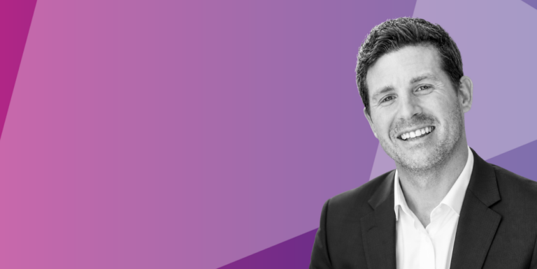 A man in a suit smiles at the camera, shown in black and white against a vibrant purple geometric background.