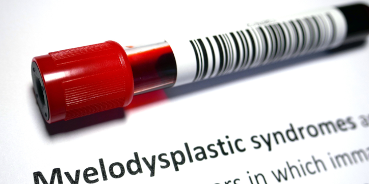 A blood sample tube with a red cap lies on a document that partially reads Myelodysplastic syndromes. The image suggests a connection to medical testing or diagnosis for this condition.