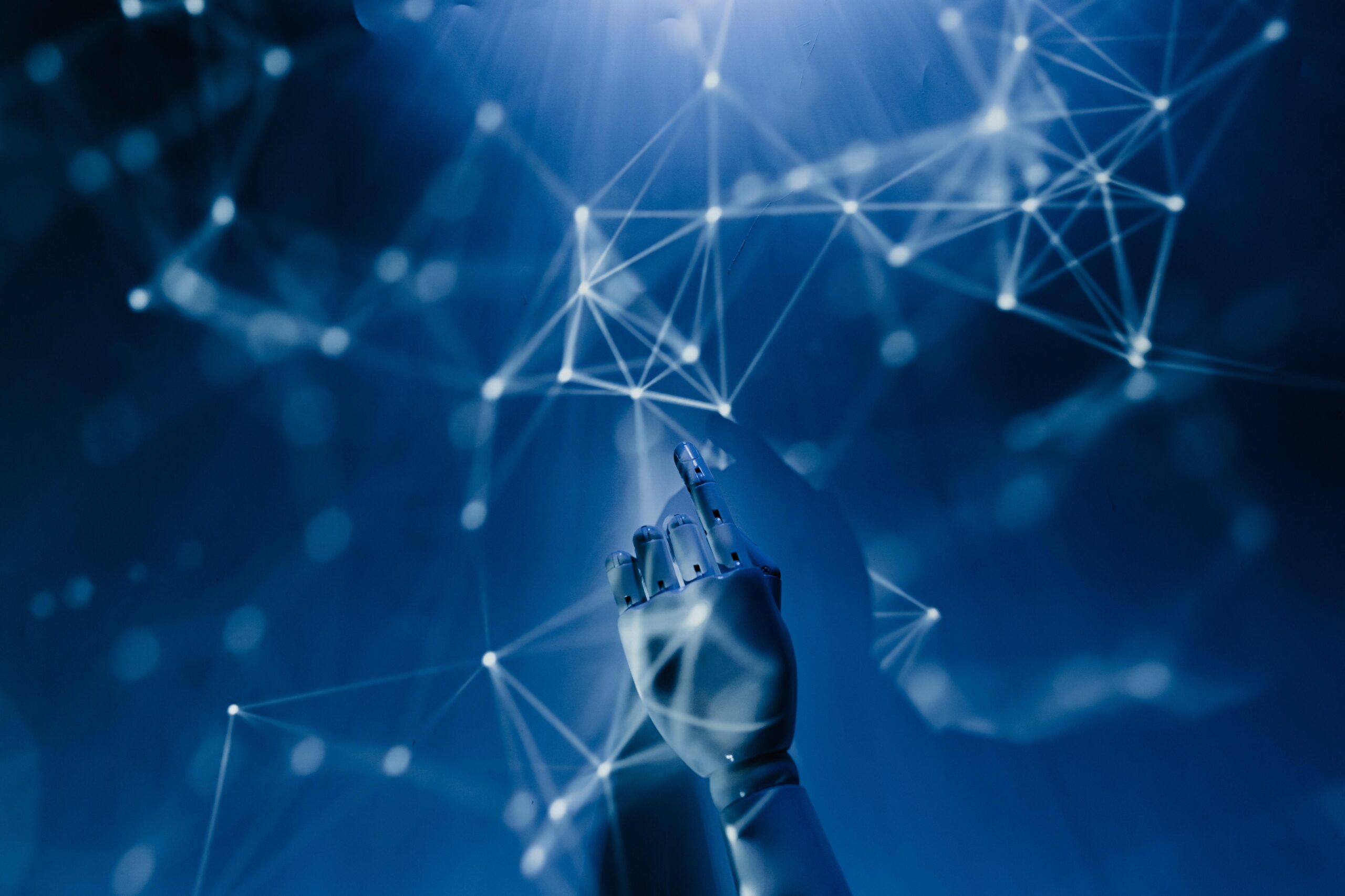 A robotic hand points upwards towards a glowing network of interconnected lines and nodes on a blue background, symbolising artificial intelligence and technology.